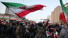A member of Iran's riot police waves a national flag stands as fans celebrate their football team's win against Wales during the Qatar 2022 World Cup, in the capital Tehran on November 25, 2022. - Iran struck twice in the dying moments of added time to earn a 2-0 win over 10-man Wales in their Group B clash at the World Cup today. Rouzbeh Cheshmi and Ramin Rezaeian scored to give Iran a famous win, which moved them into second place in the group behind England, who face the USA later in the day. (Photo by Atta KENARE / AFP)