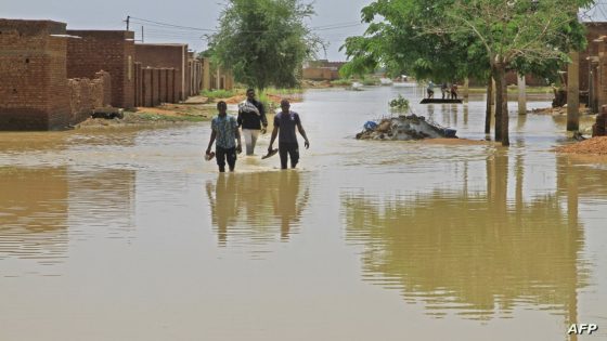 People wade through flood water in Managil city in al-Gezira state, around 250Km south of the capital, on August 23, 2022. - Sudan declared a state of emergency due to floods in six states, including River Nile. Since the start of the devastating rainy season, thousands of Sudanese families have been left homeless, sheltering under tattered sacking. (Photo by Ebrahim Hamid / AFP)